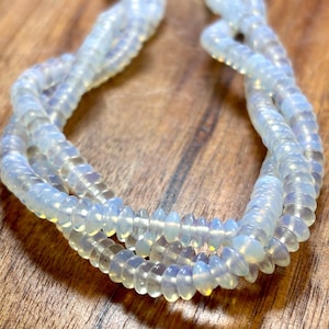 May include: A strand of translucent, milky white opal-like beads with a soft iridescent sheen. The beads are small, round, and disc-shaped, strung together in a continuous loop. The material has a smooth, polished finish that catches light.