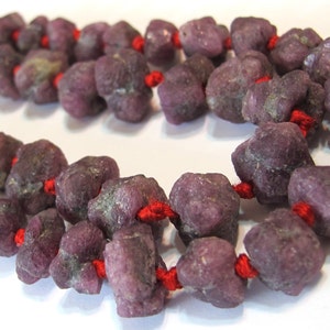 May include: A strand of purple gemstone beads strung together with red thread. The beads are rough and irregular in shape, giving the necklace a rustic look.