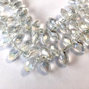 May include: A strand of clear faceted crystal beads in a teardrop shape. The beads are strung on a thin wire and are arranged in a loose, flowing pattern.