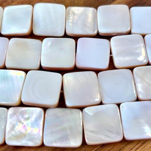 May include: A strand of white square-shaped shell beads. The beads have a pearlescent finish and are strung on a clear thread.
