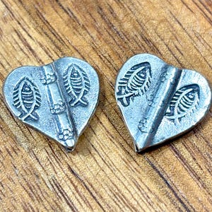 May include: Two silver-toned heart-shaped pendants. Each pendant features two fish and a bamboo stalk design. The pendants are displayed on a wooden surface.