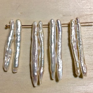 May include: A collection of six white baroque pearls, each with a unique irregular shape and a smooth, lustrous surface. The pearls are strung on a thin wire and are ready to be used in jewelry making.
