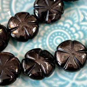 May include: A close-up of black gemstone beads with a starburst design. The beads are smooth and shiny, and they are arranged in a row on a blue and white patterned surface.