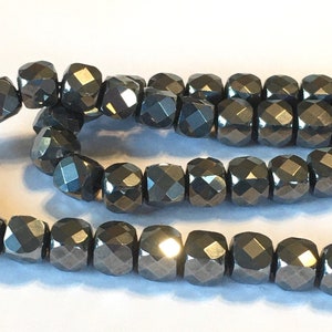 May include: A strand of dark gray faceted beads. The beads are round and have a shiny finish.