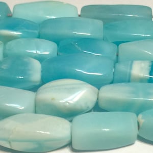 May include: Close-up of a collection of polished, rectangular beads in varying shades of light blue and white. The beads have a smooth, glossy finish and are strung together, suggesting they are for jewelry making or crafts.