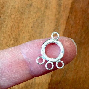 May include: Silver-toned metal connector with a round loop and three smaller loops extending from the bottom. The connector is designed for attaching jewelry pieces.