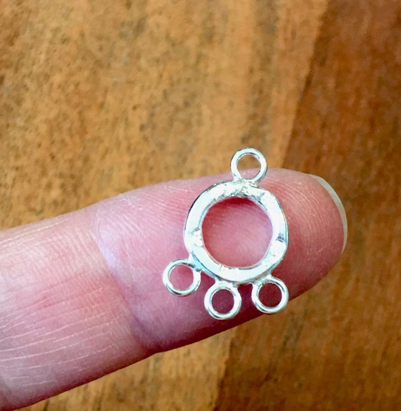 May include: Silver-toned metal connector with a round loop and three smaller loops extending from the bottom. The connector is designed for attaching jewelry pieces.