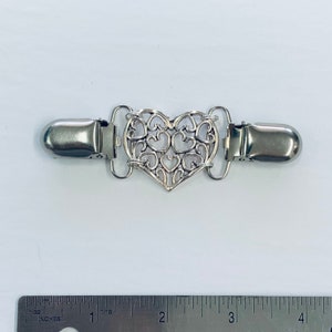 May include: Silver-toned heart-shaped clasp with a delicate filigree design. The clasp is approximately 2 inches long and has two metal clips on either end.