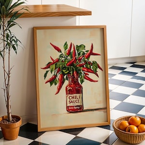 Może przedstawiać: Oprawiony wydruk przedstawiający czerwone papryczki chili ułożone w butelce z napisem "Chili Sauce Extra Spicy". Grafika ma jasne tło i drewnianą ramę. Roślina doniczkowa i kosz pomarańczy znajdują się na pierwszym planie.