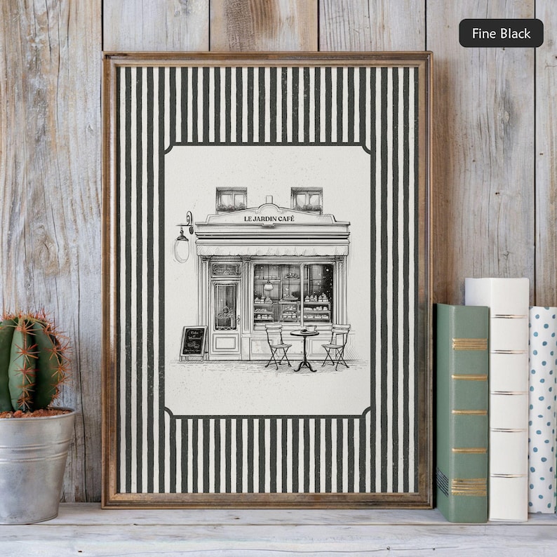 May include: Framed black and white print of a cafe, "Le Jardin Cafe", with a striped border. The print is displayed on a wooden shelf with books and a cactus in a metal pot. The cafe illustration shows tables, chairs, and a menu board.
