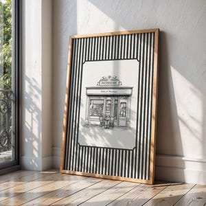 May include: Framed black and white print of a patisserie shop with the word "PATISSERIE" above the entrance. The print is in a wooden frame and has a black and white striped border.