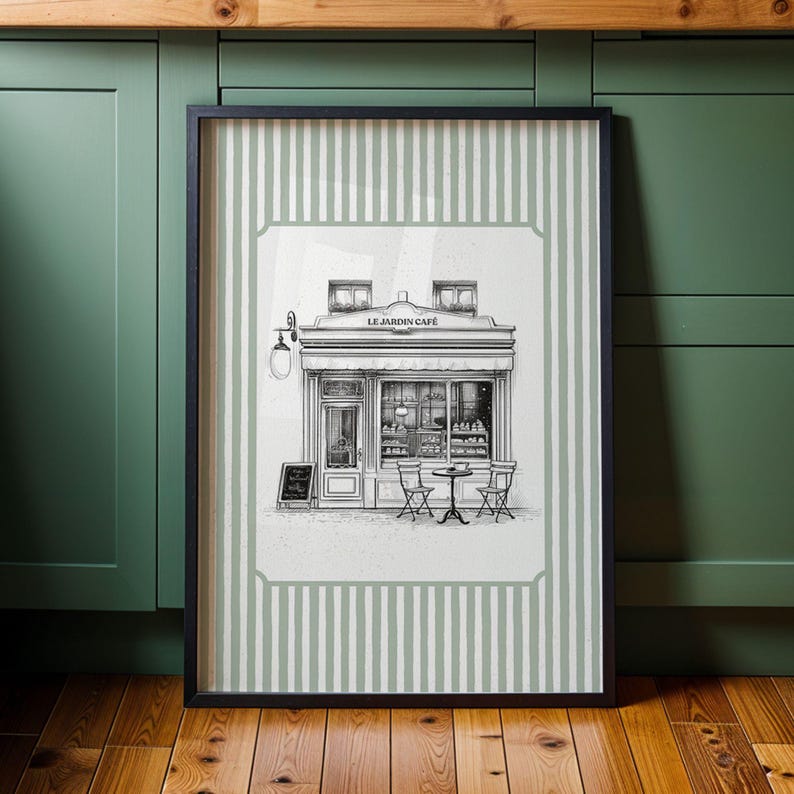 May include: Black framed print of a cafe scene. The artwork depicts a detailed black and white illustration of a cafe exterior with tables and chairs. The print is set against a background of vertical green and white stripes.