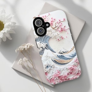 Puede incluir: Una funda de teléfono blanca con un diseño de arte en papel 3D de una ola y flores de cerezo. La ola es azul y blanca, y las flores de cerezo son rosas y blancas.