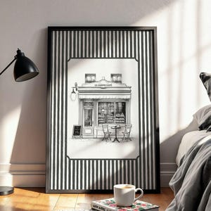 May include: Black and white framed print of a cafe scene. The artwork features a detailed illustration of a cafe with outdoor seating, a sign, and the text "LE JARDIN CAFE". The frame has a black and white striped border.