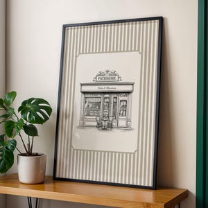 May include: Framed black and white illustration of a French patisserie. The artwork features a detailed drawing of a bakery storefront with the word "PATISSERIE" above the entrance. The print is set against a striped background.