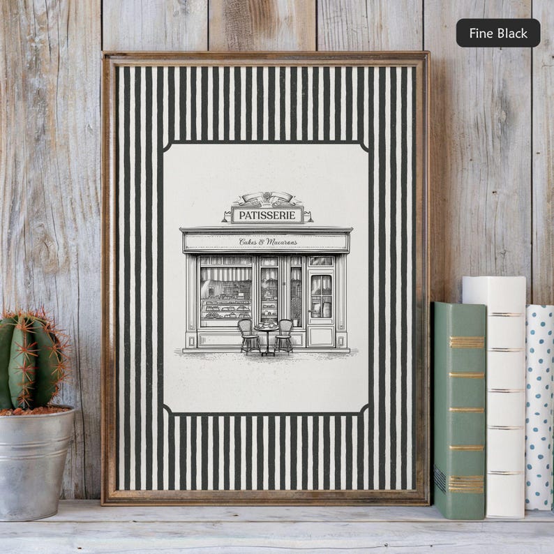 May include: Framed black and white print of a patisserie shop with the word "PATISSERIE" above the entrance. The frame is a light brown color and has a black and white striped border. The print is displayed on a wooden surface.