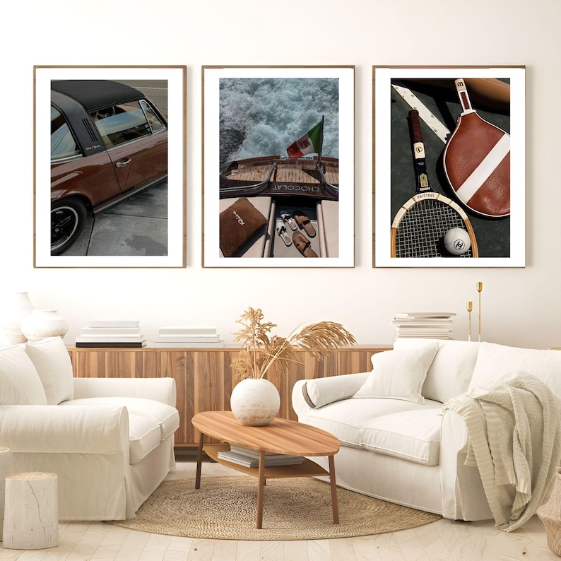 May include: Three framed art prints. The left print shows a brown car with a black roof. The centre print depicts a boat with an Italian flag. The right print displays a tennis racket, ball, and paddle.