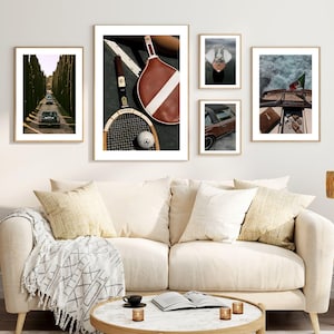 May include: A set of framed art prints showcasing classic cars, tennis gear, a boat, and a person in a boat. The prints are hung above a cream sofa with cushions and a patterned throw. A round coffee table with candles and books sits in front of the sofa.