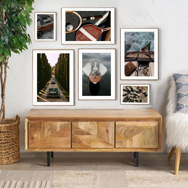 May include: A gallery wall of framed art prints. The images depict a classic car, tennis equipment, a boat, a tree-lined road, and a selection of shoes. The frames are gold, and the art is displayed above a wooden cabinet with black metal legs.