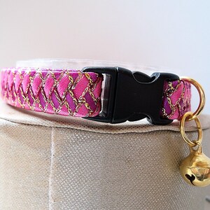 May include: Pink and gold cat collar with a black buckle and a gold bell.