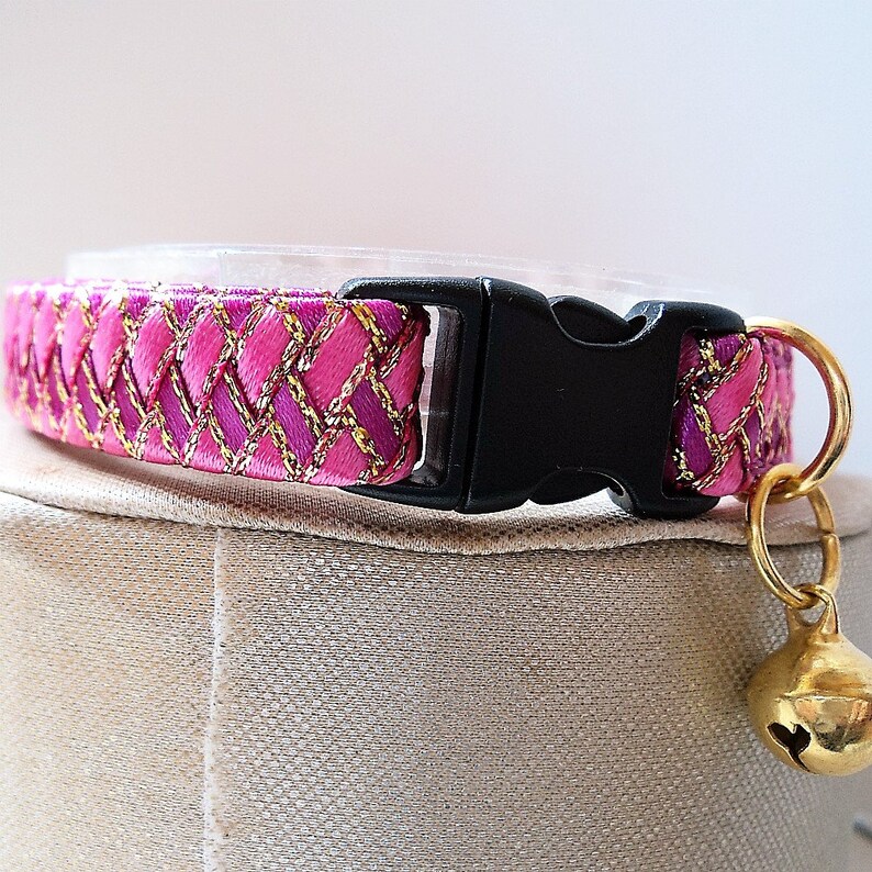 May include: Pink and gold cat collar with a black buckle and a gold bell.