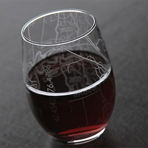 May include: A clear glass wine glass with an etched map design. The glass is filled with red wine. The map coordinates are visible on the glass: 42.4542, 76.4786.