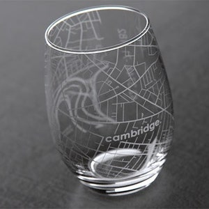 May include: A clear glass wine glass with an etched design of the city of Cambridge, Massachusetts. The glass has a rounded bottom and a wide rim.