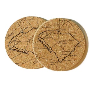 May include: Two cork coasters featuring an outline map of South Carolina with the state name printed in black. The map includes major cities and towns.