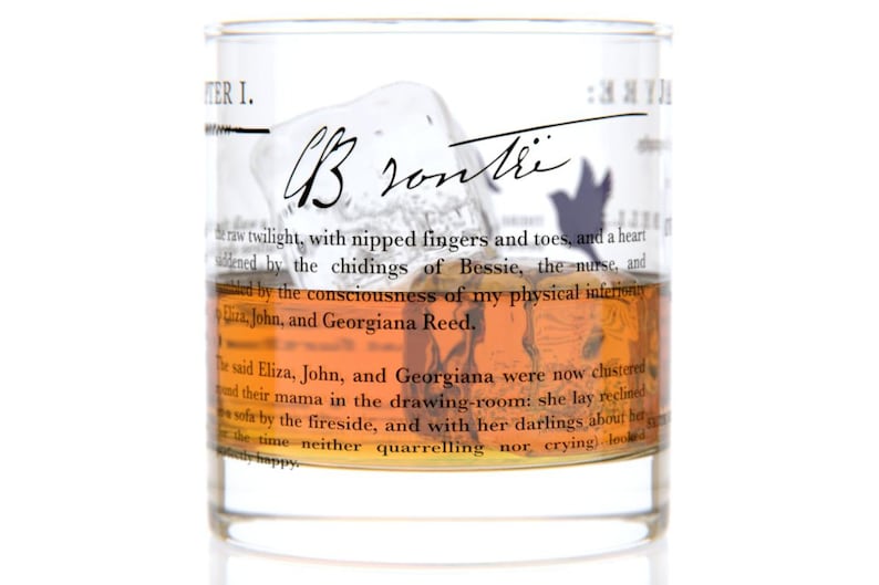 May include: A clear glass tumbler with a brown liquid inside. The glass has text printed on it, including the words "Chapter I." and "Brontre".