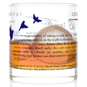May include: A clear glass with a brown liquid inside. The glass has a quote from "Jane Eyre" printed on it. The quote reads: "THERE was no possibility of taking a walk that day. We had been wandering, indeed, in the leafless shrubbery an hour in the morning; but since dinner (Mrs. Reed, when there was no company, dined early) the cold winter wind had brought with it clouds so sombre, and a rain so penetrating, that further out-door exercise was now out of the question. I was glad of it: I never liked long walks, especially afternoons: dreadful to me was the coming"
