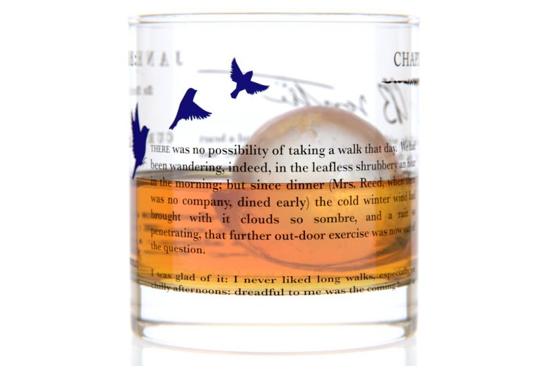 May include: A clear glass with a brown liquid inside. The glass has a quote from "Jane Eyre" printed on it. The quote reads: "THERE was no possibility of taking a walk that day. We had been wandering, indeed, in the leafless shrubbery an hour in the morning; but since dinner (Mrs. Reed, when there was no company, dined early) the cold winter wind had brought with it clouds so sombre, and a rain so penetrating, that further out-door exercise was now out of the question. I was glad of it: I never liked long walks, especially afternoons: dreadful to me was the coming"
