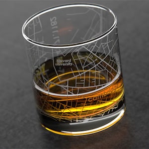 May include: A clear glass with an etched design of the streets of Cambridge, Massachusetts. The glass is filled with a golden brown liquid and the text "harvard university." and "cambridge" are visible.