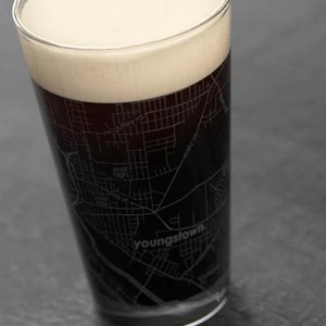 May include: A pint glass with a black and white map of Youngstown, Ohio, etched into the side. The glass is filled with a dark beer with a thick head of foam.