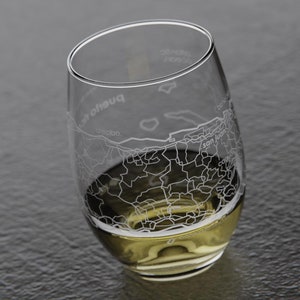 May include: A clear glass wine glass with an etched design of the city of San Juan, Puerto Rico. The glass is filled with a light yellow liquid.