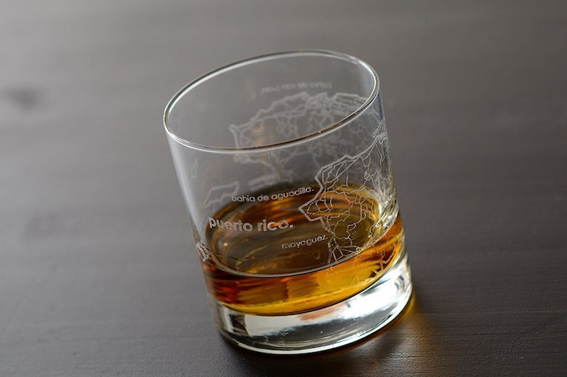 May include: A clear glass with an etched map of Puerto Rico and the words "puerto rico." The glass is filled with amber-colored liquid.