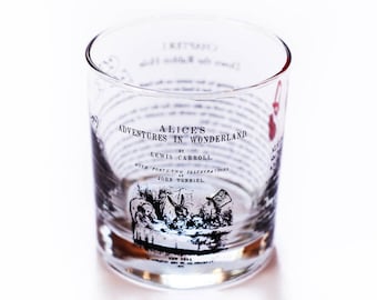 May include: A clear glass tumbler with black text and an illustration from Alice's Adventures in Wonderland by Lewis Carroll. The text reads "Alice's Adventures in Wonderland by Lewis Carroll with forty-two illustrations by John Tenniel."