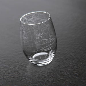 Op de afbeelding: Een helder glazen wijnglas met een gegraveerde kaart van Boston, Massachusetts. De kaart bevat de tekst "boston 26.2" en "Framingham Heart Study".