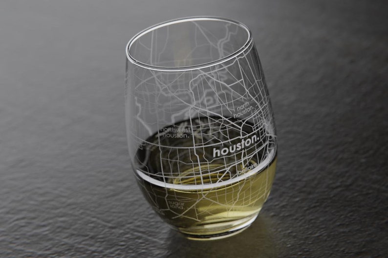 May include: A clear glass wine glass with an etched design of the Houston, Texas street map. The glass is filled with a light yellow liquid.