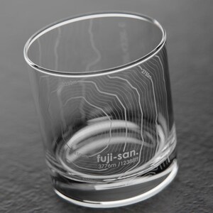 May include: A clear glass tumbler with an etched design of Mount Fuji, Japan. The glass features the text "fuji-san. 3776m / 12388ft".