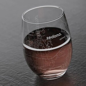 May include: A clear glass wine glass with a design of the city of Sedona, Arizona etched on the side. The glass is filled with red wine.