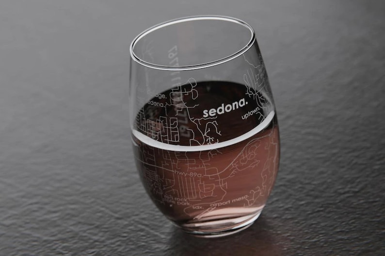 May include: A clear glass wine glass with a design of the city of Sedona, Arizona etched on the side. The glass is filled with red wine.
