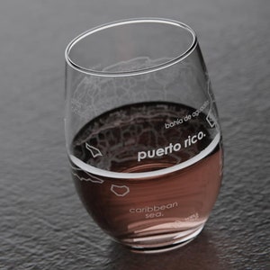 May include: A clear glass wine glass with an etched map of Puerto Rico. The glass is filled with a red liquid and the text "puerto rico." is visible on the glass.