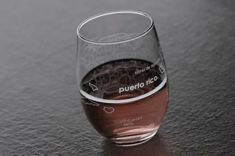 May include: A clear glass wine glass with an etched map of Puerto Rico. The glass is filled with a red liquid and the text "puerto rico." is visible on the glass.