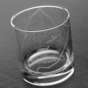 May include: Clear glass tumbler etched with a detailed map of Riverside, California. The map includes street names and landmarks. The glass has a simple, elegant design, perfect for serving beverages. The word "Riverside" is etched on the glass.