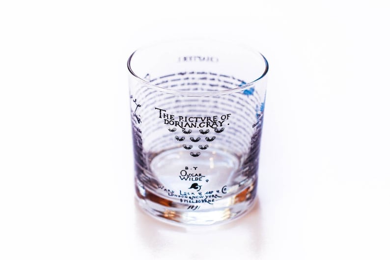 May include: A clear glass tumbler with black text that reads "The Picture of Dorian Gray" by Oscar Wilde. The text is wrapped around the glass.