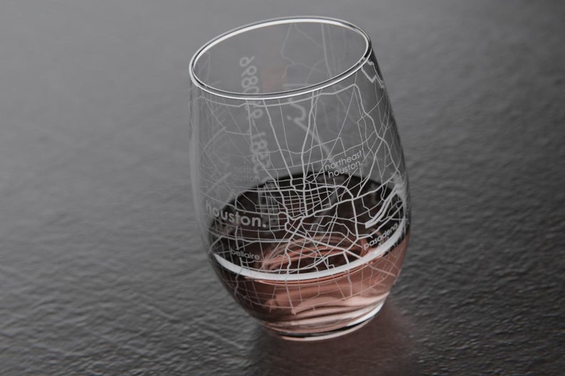 May include: A clear glass wine glass with an etched design of the Houston, Texas street map. The glass is filled with a pink beverage.
