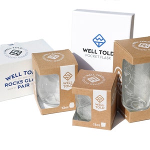 May include: Three cardboard boxes with brown and white labels. The boxes contain a set of two 12-ounce rocks glasses and a 16-ounce glass. The boxes have the text "Well Told" and a logo of a mountain with a blue river.