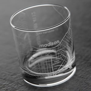 May include: A clear glass tumbler with an etched design of the city of Madison, Wisconsin. The design includes street names and landmarks, such as the Capitol Building and the University of Wisconsin campus.