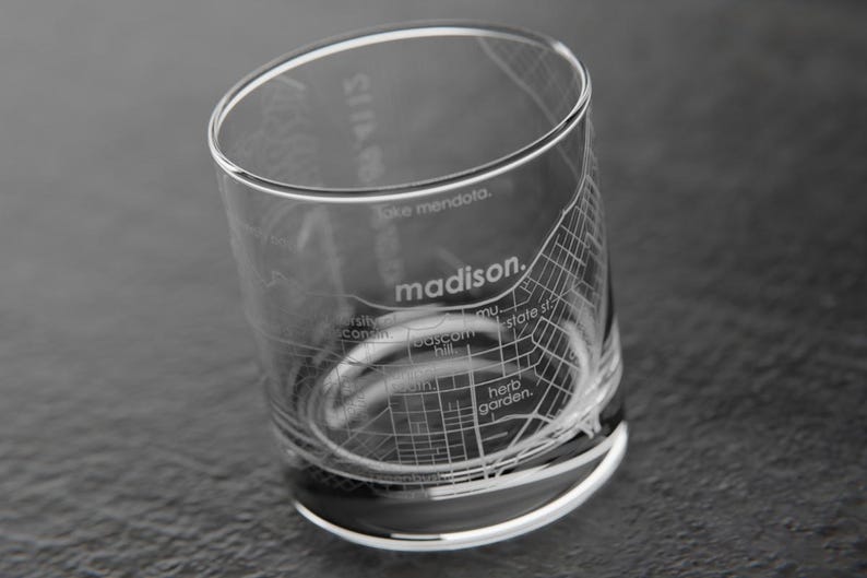 May include: A clear glass tumbler with an etched design of the city of Madison, Wisconsin. The design includes street names and landmarks, such as the Capitol Building and the University of Wisconsin campus.