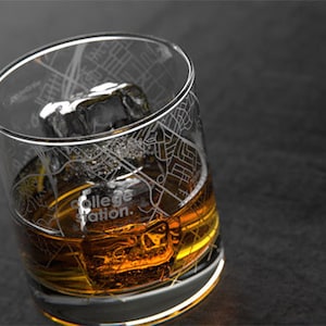 May include: A clear glass with an etched map of College Station, Texas, filled with amber liquid and an ice cube.